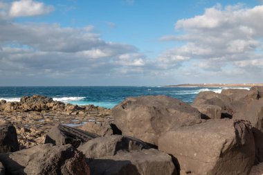 Küçük dalgalarla Atlantik Okyanusu 'nun kayalık kıyıları. Volkanik kayalar koyu kahverengiden siyah renge. Beyaz bulutlu mavi gökyüzü. Santa, Lanzarote, Kanarya Adaları, İspanya.