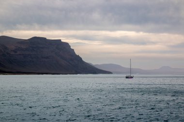 Adanın kuzeyindeki kayalıklardan ve volkanik kayalıklardan bir tekne görüntüsü. Küçük tekne. Kışın beyaz bulutlu mavi gökyüzü. Mirador del Rio, Lanzarote, Kanarya Adaları, İspanya.