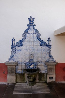 Duvarında su musluğu hakkında dekoratif bir Azulejos olan bir sokak. Beyaz cephe ve kırmızı taban. Funchal Caddesi, Madeira, Portekiz.