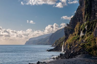 Atlantik Okyanusu kıyısındaki volkanik kayalıklar. Beyaz bulutlu mavi gökyüzü. Ponta do Sol, Madeira, Portekiz.