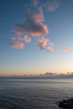 İskelenin bir parçası olarak taşları. Gün batımında sakin bir Atlantik okyanusu. Gökyüzünde pembe bulutlar. Ponta do Sol, Madeira, Portekiz.