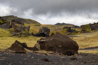 Çeşitli şekillerdeki volkanik kayaların ayrıntıları kısmen yosun ve liken ile kaplı. Beyaz bulutlu mavi gökyüzü. Katla geopark, İzlanda.