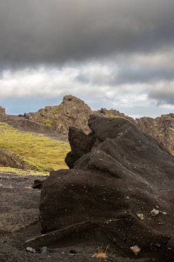 Çeşitli şekillerdeki volkanik kayaların ayrıntıları kısmen yosun ve liken ile kaplı. Beyaz bulutlu mavi gökyüzü. Katla geopark, İzlanda.