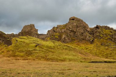 Çeşitli şekillerdeki volkanik kayaların ayrıntıları kısmen yosun ve liken ile kaplı. Beyaz bulutlu mavi gökyüzü. Katla geopark, İzlanda.