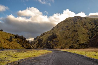 Sonbaharda kadife bir yüzeye sahip olan volkanik kayalar ve dağlar, yeşil yosun, liken ve çimenler sayesinde sarı renge kavuştu. Beyaz bulutlu mavi gökyüzü. Taşra yolu. Katla geopark, İzlanda.