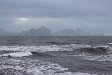 View from Iceland on islands Heimaey on the horizon. Waves of Atlantic ocean. Cloudy rainy sky. Landeyjahofn, Iceland. clipart