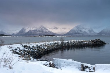 Karla kaplı bir manzara. Dağlar ve Kvaerfjord 'un suyu. Güneşin doğuşu / batışı sırasında bulutlu bir gökyüzü. Harstad, Norveç.