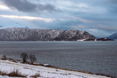 Karla kaplı bir manzara. Dağlar ve Kvaerfjord 'un suyu. Güneşin doğuşu / batışı sırasında bulutlu bir gökyüzü. Harstad, Norveç.