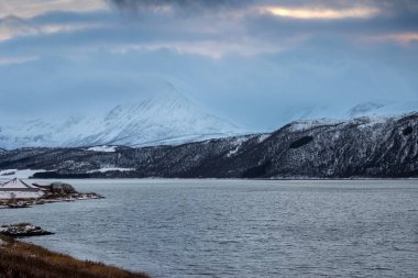 Karla kaplı bir manzara. Dağlar ve Kvaerfjord 'un suyu. Güneşin doğuşu / batışı sırasında bulutlu bir gökyüzü. Harstad, Norveç.