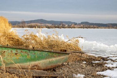 Gölet (baraj) Lipno, kıyı şeridindeki buz için çok küçük ve donuk olduğunda. Sahilde bir tekne. Arka planda dağlar. Horni Plana, Çek repbulik.