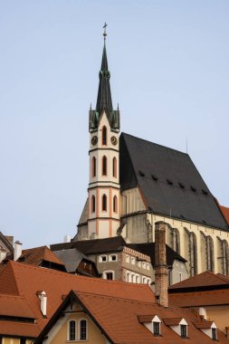 Tepedeki Gotik Aziz Vitus Kilisesi, eski şehirdeki evlerin çatılarıyla çevrili. Mavi kış gökyüzü. Cesky Krumlov, Çek Cumhuriyeti.