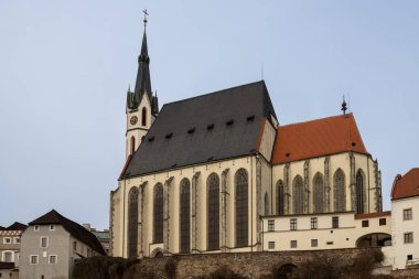 Tepedeki Gotik Aziz Vitus Kilisesi, eski şehirdeki evlerin çatılarıyla çevrili. Mavi kış gökyüzü. Cesky Krumlov, Çek Cumhuriyeti.