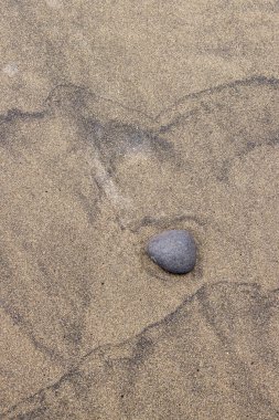 Sarı ve koyu volkanik kumların yapısı soyut dokular yaratıyor, bir çakıl taşıyla birlikte. El Burrero, Las Palmas, Gran Kanarya, Kanarya Adaları, İspanya.