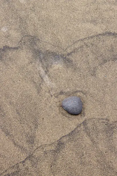 Sarı ve koyu volkanik kumların yapısı soyut dokular yaratıyor, bir çakıl taşıyla birlikte. El Burrero, Las Palmas, Gran Kanarya, Kanarya Adaları, İspanya.