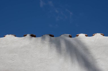 Palmiye yaprağı gölgesinde beyaz çit. Kenarları süslenmiş. Açık beyaz bulutlu mavi gökyüzü. Maspalomalar, San Bartolome de Tirajana, Las Palmas, Gran Canaria, Kanarya Adaları, İspanya.