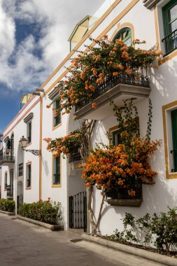 Dar sokaklar renkli detaylarla ve kışın açan bitkilerle dolu beyaz evlerle dolu. Beyaz bulutlu mavi gökyüzü. Puerto de Mogan, Las Palmas, Gran Canaria, Kanarya Adaları, İspanya.