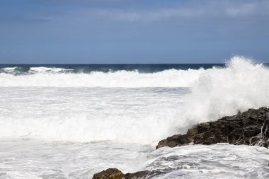 Atlantik Okyanusu kıyısındaki volkanik siyah kayalar. Kış rüzgarlı bir günde yoğun dalgalar. Beyaz bulutlu mavi gökyüzü. Las Palmas, Gran Canaria, Kanarya Adaları, İspanya.