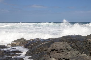 Atlantik Okyanusu kıyısındaki volkanik siyah kayalar. Kış rüzgarlı bir günde yoğun dalgalar. Beyaz bulutlu mavi gökyüzü. Las Palmas, Gran Canaria, Kanarya Adaları, İspanya.
