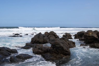 Atlantik Okyanusu kıyısındaki volkanik siyah kayalar. Kış rüzgarlı bir günde yoğun dalgalar. Beyaz bulutlu mavi gökyüzü. Las Palmas, Gran Canaria, Kanarya Adaları, İspanya.