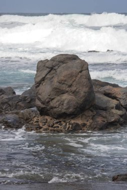 Atlantik Okyanusu kıyısındaki volkanik siyah kayalar. Kış rüzgarlı bir günde yoğun dalgalar. Beyaz bulutlu mavi gökyüzü. Las Palmas, Gran Canaria, Kanarya Adaları, İspanya.