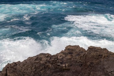 Atlantik Okyanusu kıyısındaki volkanik kahverengi kayalar. Kış rüzgarlı bir günde yoğun dalgalar. Galdar, Las Palmas, Gran Kanarya, Kanarya Adaları, İspanya.