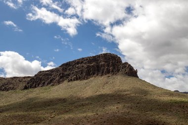 Majestic Dağı, gelecek baharda taze yeşilliklerle kaplanacak. Beyaz bulutlu mavi gökyüzü. Roque de Los Cardones, Aguimes, Las Palmas, Gran Canaria, Kanarya Adaları, İspanya.