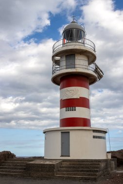 Deniz feneri (Faro de Arinaga) kırmızı ve beyaz çizgili, geleneksel tarzda. Beyaz bulutlu mavi gökyüzü. Atlantik Okyanusu kıyısında. Arinaga, Las Palmas, Gran Canaria, Kanarya Adaları, İspanya.