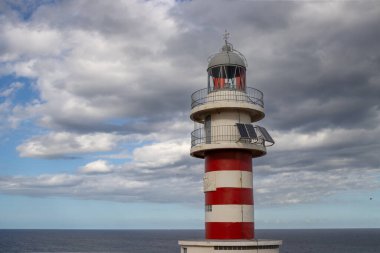 Deniz feneri (Faro de Arinaga) kırmızı ve beyaz çizgili, geleneksel tarzda. Beyaz bulutlu mavi gökyüzü. Atlantik Okyanusu kıyısında. Arinaga, Las Palmas, Gran Canaria, Kanarya Adaları, İspanya.