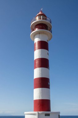 Deniz feneri (Faro de Sardina) kırmızı ve beyaz çizgili, geleneksel tarzda. Mavi gökyüzü. Atlantik Okyanusu kıyısında. Galdar, Las Palmas, Gran Kanarya, Kanarya Adaları, İspanya.