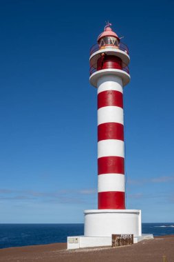 Deniz feneri (Faro de Sardina) kırmızı ve beyaz çizgili, geleneksel tarzda. Mavi gökyüzü. Atlantik Okyanusu kıyısında. Galdar, Las Palmas, Gran Kanarya, Kanarya Adaları, İspanya.