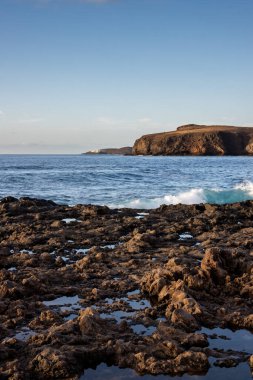 Atlantik Okyanusu 'nun Rocky sahilleri. Rüzgarlı bir kış günü dalgalar. Arka plandaki dağ. Beyaz bulutlu mavi gökyüzü. Puerto de las Nieves, Las Palmas, Gran Canaria, Kanarya Adaları, İspanya.