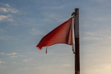 Atlantik Okyanusu sahilinde dalgalanan kırmızı bayrak. Akşamüstü bulutlu mavi gökyüzü. Puerto de las Nieves, Las Palmas, Gran Canaria, Kanarya Adaları, İspanya.