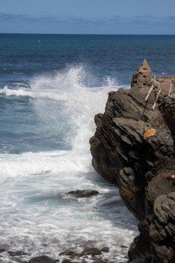 Kıyı kayaları ve Atlantik Okyanusu 'nun koyu mavi suları, rüzgarlı bir kış gününde dalgalanan dalgalar. Mavi gökyüzü ve ışık bulutları. Quintanilla, Las Palmas, Gran Canaria, Kanarya Adaları, İspanya.