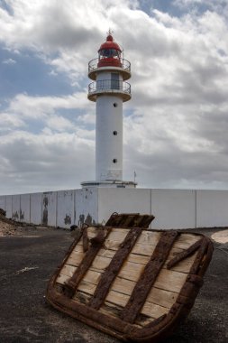 Beyaz yüzlü, kırmızı bluzlu, geleneksel tarzda bir deniz feneri. Yoğun bulutlu mavi gökyüzü. Atlantik Okyanusu kıyısında. Taliarte, Las Palmas, Gran Canaria, Kanarya Adaları, İspanya.