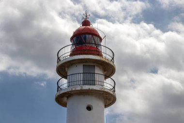 Beyaz yüzlü, kırmızı bluzlu, geleneksel tarzda bir deniz feneri. Yoğun bulutlu mavi gökyüzü. Atlantik Okyanusu kıyısında. Taliarte, Las Palmas, Gran Canaria, Kanarya Adaları, İspanya.
