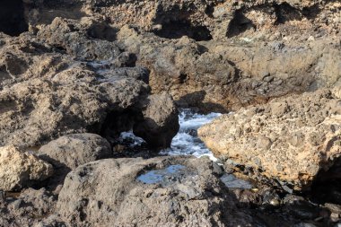Ortasında bir delik olan, Atlantik okyanus dalgalarının sıçradığı büyük, dalgalı kıyı kayaları. Telde, Las Palmas, Gran Canaria, Kanarya Adaları, İspanya.
