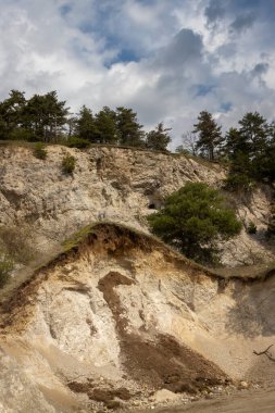 Kum taşı ocağının olduğu bir tepenin kalan kısmı. Tepede yetişen kozalaklı ağaçlar. Yoğun beyaz bulutlu mavi gökyüzü. Trstin, Slovakya Cumhuriyeti.