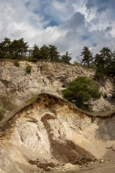 Kum taşı ocağının olduğu bir tepenin kalan kısmı. Tepede yetişen kozalaklı ağaçlar. Yoğun beyaz bulutlu mavi gökyüzü. Trstin, Slovakya Cumhuriyeti.