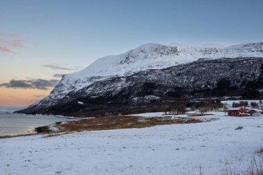 Karada sonbahar karı. Arka planda büyük bir dağ. Güneşin doğuşunda renkli bir gökyüzü. Norveç Denizi 'nin suyu. Sert Stad, Norveç.