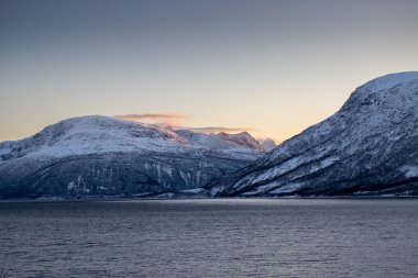 Norveç 'in sakin denizi ve dağları sonbaharda ince kar tabakalarıyla kaplıdır. Güneş doğarken renkli bulutlar. Harstad, Norveç.