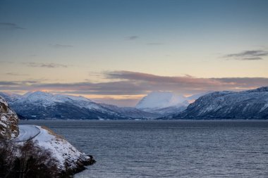 Norveç 'in sakin denizi ve dağları sonbaharda ince kar tabakalarıyla kaplıdır. Güneş doğarken renkli bulutlar. Harstad, Norveç.