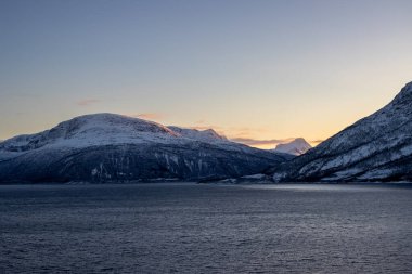 Norveç 'in sakin denizi ve dağları sonbaharda ince kar tabakalarıyla kaplıdır. Güneş doğarken renkli bulutlar. Harstad, Norveç.
