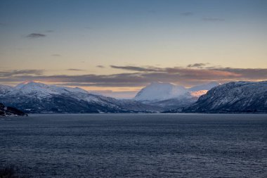 Norveç 'in sakin denizi ve dağları sonbaharda ince kar tabakalarıyla kaplıdır. Güneş doğarken renkli bulutlar. Harstad, Norveç.