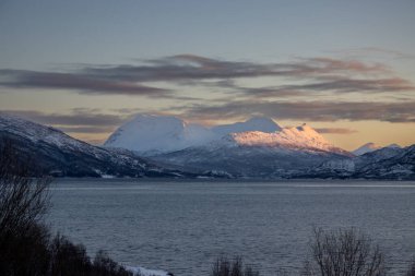 Sakin Atlantik Okyanusu. Sonbaharın sonlarında karlı doğa. Arka plandaki dağ. Güneşin doğuşunda bulutlu gökyüzü. Hamnvik, Norveç.
