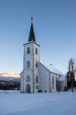 Yüksek kulesi olan Lüteriyen bir kilisenin beyaz binası. Sonbaharın sonlarında kar. Mavi gökyüzü. Ibestad, Norveç.