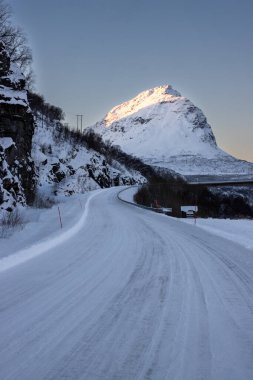 Doğa, yol ve arka plandaki yüksek dağ, sonbaharın sonlarında her şey karla kaplıydı. Mavi gökyüzü. Krakohamn, Norveç.