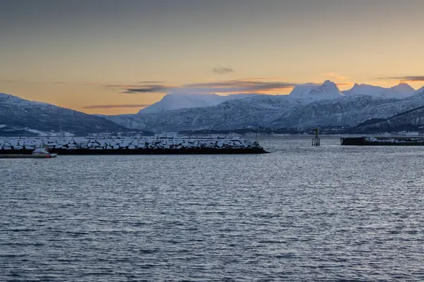 Arka planda doğa ve yüksek dağlar, sonbaharın sonlarında her şey karla kaplıydı. Norveç denizinin sakin suları. Güneş doğarken gökyüzü rengarenk. Mavi gökyüzü. Hamnvik, Norveç.