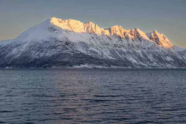 Arka planda doğa ve yüksek dağlar, sonbaharın sonlarında her şey karla kaplıydı. Norveç denizinin sakin suları. Güneş doğarken altın tepeler. Mavi gökyüzü. Hamnvik, Norveç.
