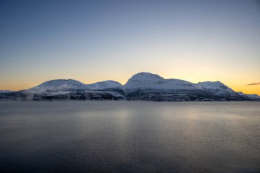 Sonbaharın sonlarında kutup günbatımında kar yağan doğa. Norveç denizinin sakin suları. Açık renkli gökyüzü ve bazı açık bulutlar. Loksebotn, Norveç.