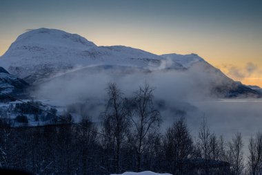 Sonbaharın sonlarında kutup günbatımında kar yağan doğa. Norveç denizinin sakin suları. Açık renkli gökyüzü ve bazı açık bulutlar. Loksebotn, Norveç.